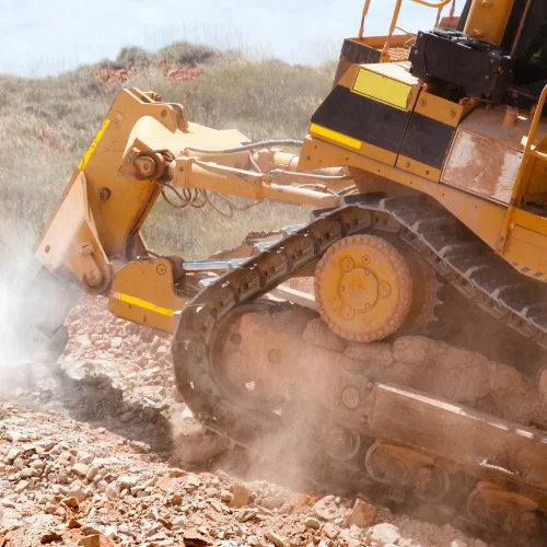 Un puissant bulldozer jaune creuse dans un sol rocheux sur un chantier de construction, soulevant de la poussière.