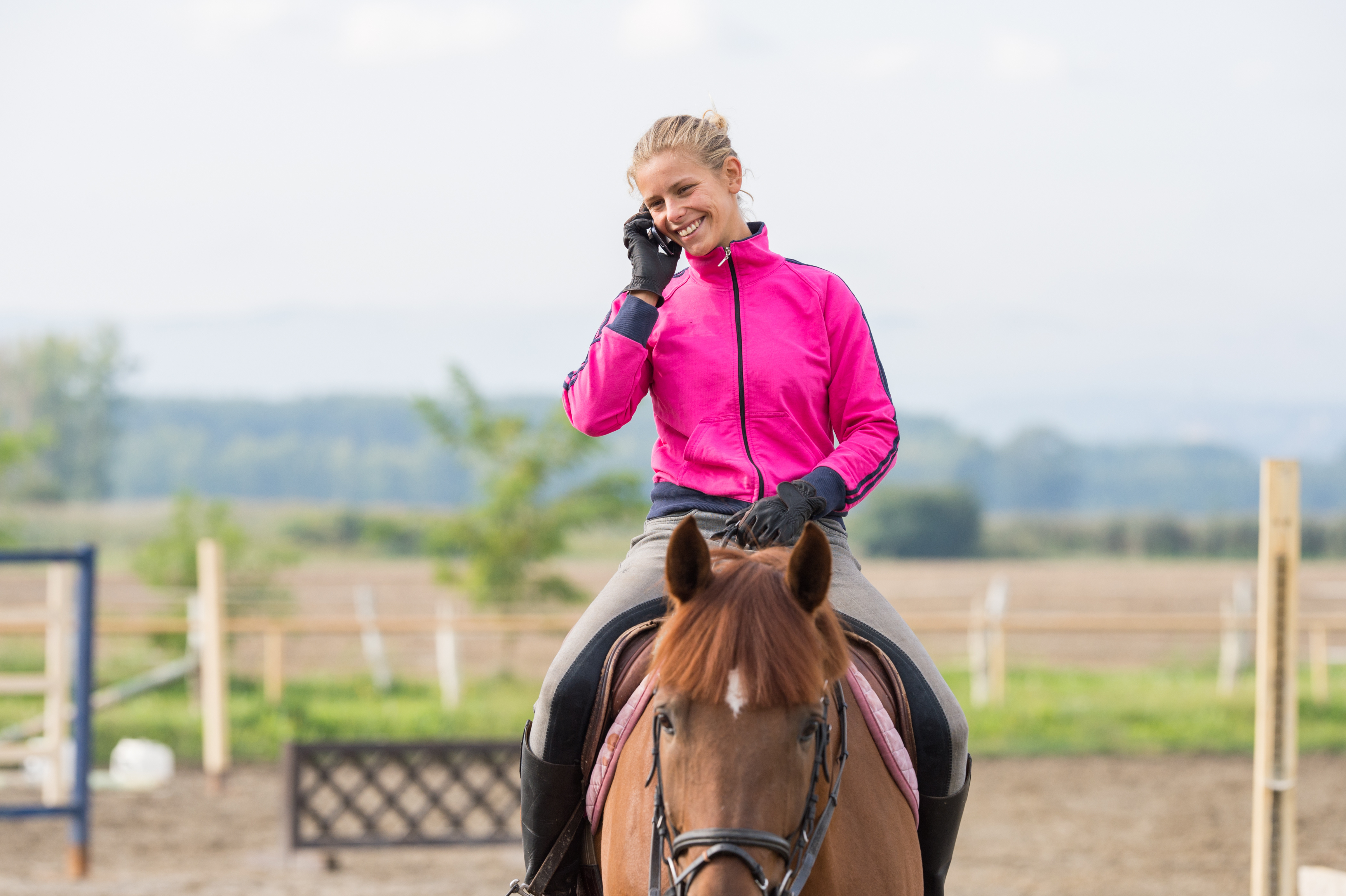 Woman smiling on horseback while speaking on phone, representing ease of scheduling and rider engagement