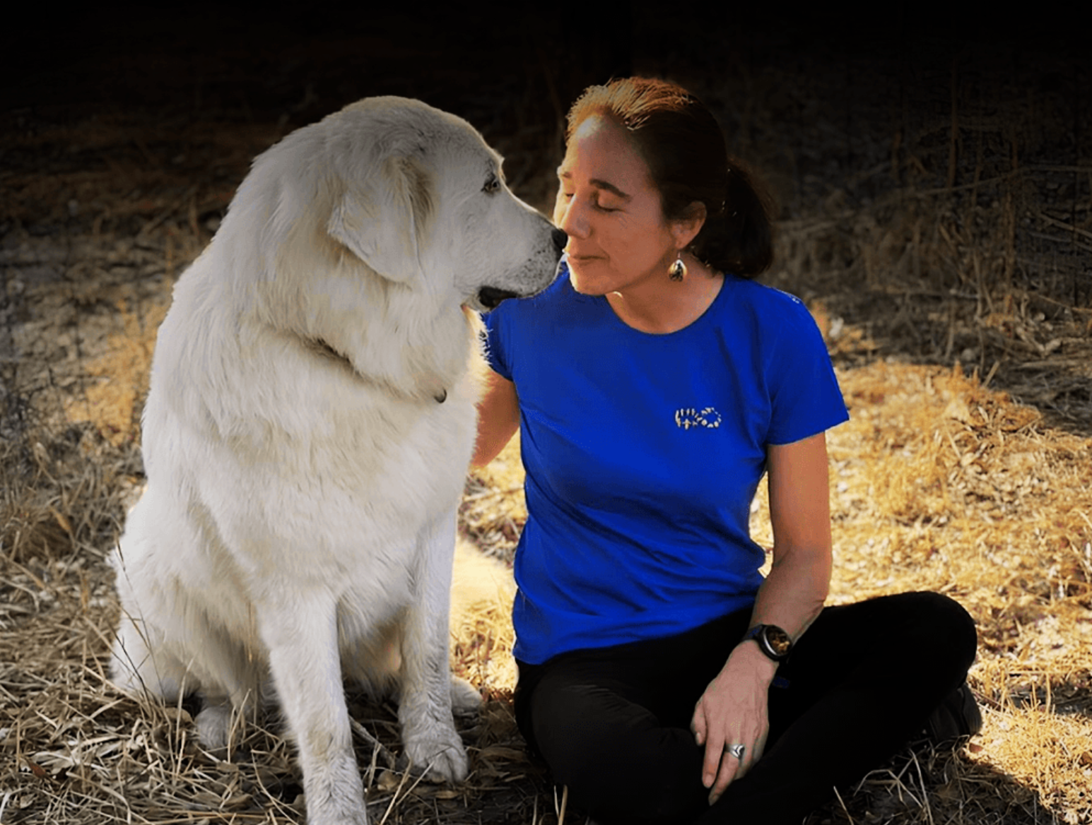 Monica seated nose-to-nose with a large white dog in sunlight, reflecting deep emotional connection and healing energy