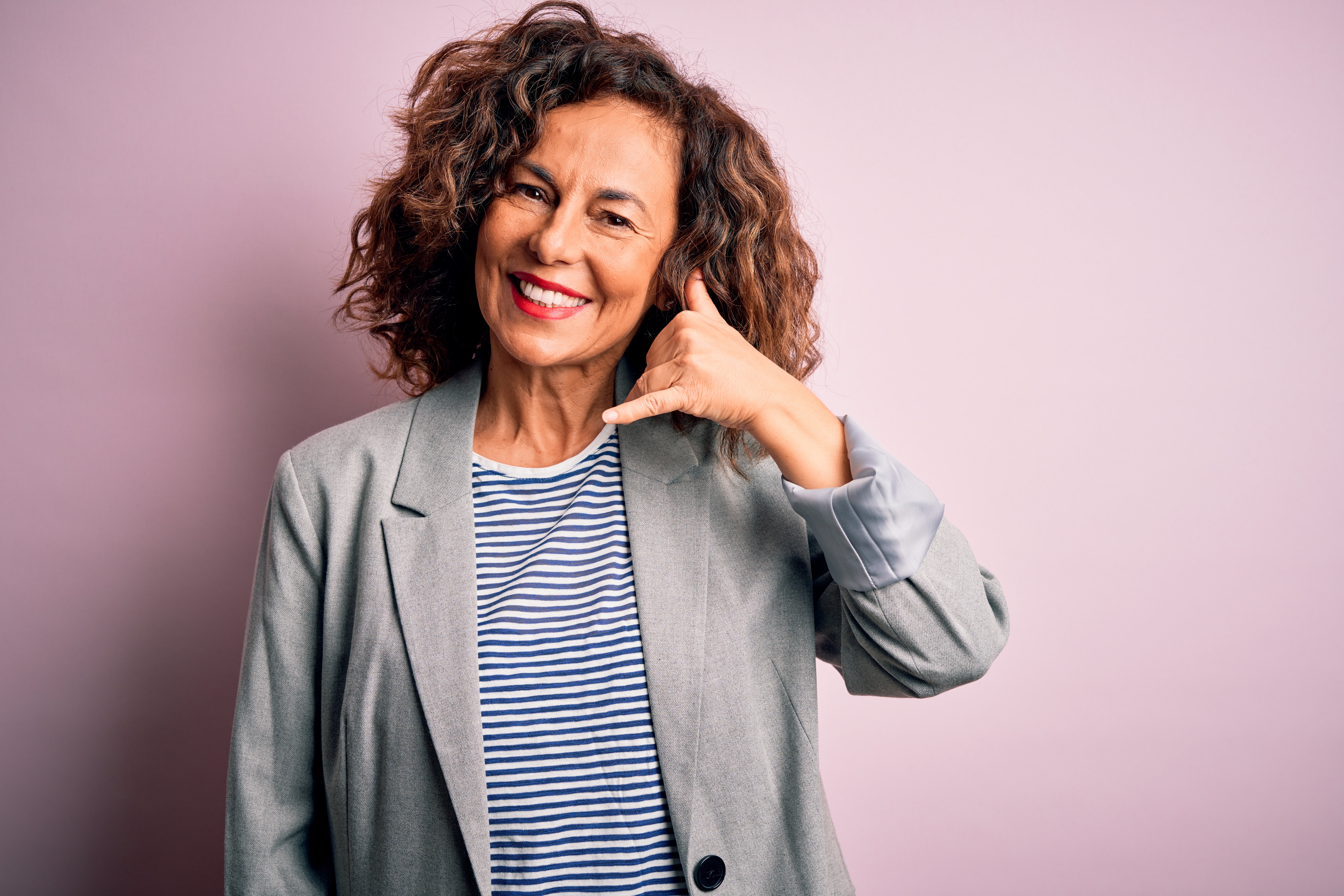Smiling woman against mauve background making a “call me” gesture, representing ongoing support and accessibility