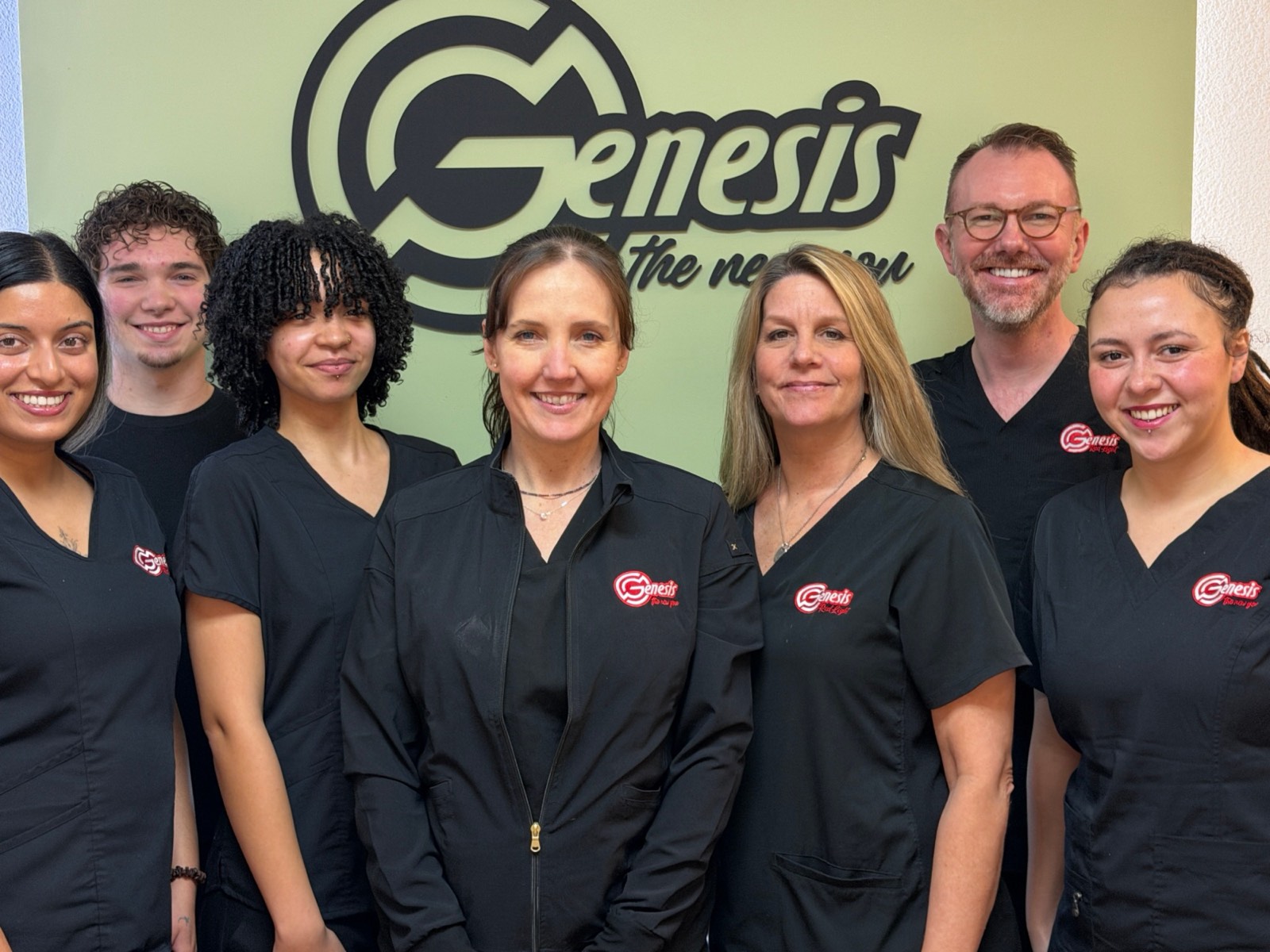 The Genesis Red Light team in front of the Genesis logo at the clinic in Cedar Park, TX