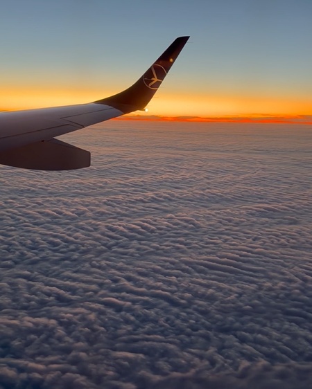 Airplane wing above the clouds at sunset