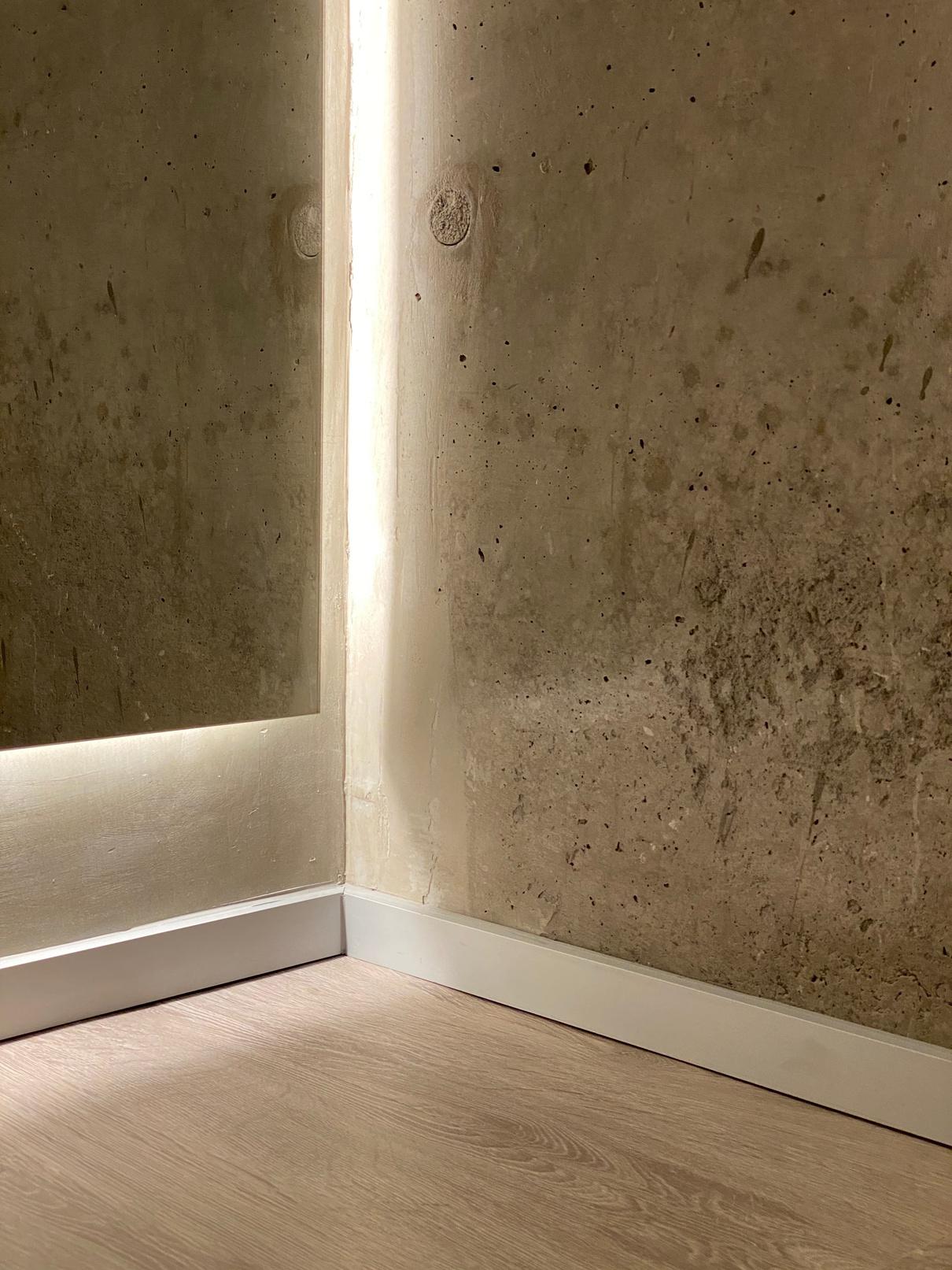 Muro de hormigón a la vista con iluminación indirecta en el cielo y guardapolvo embutido