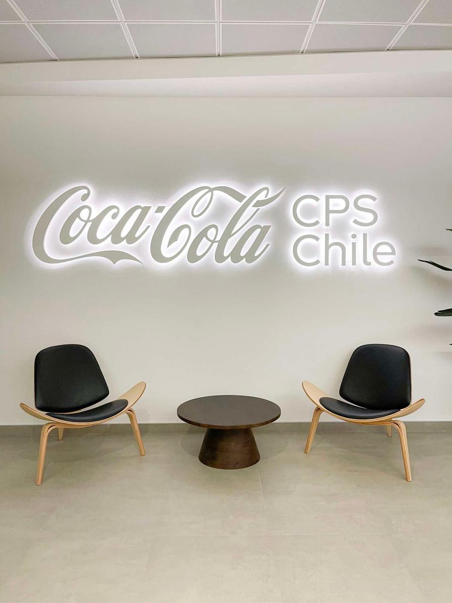 Recepción de oficinas Coca-Cola CPS Chile en San Bernardo con letrero iluminado y sillas de diseño