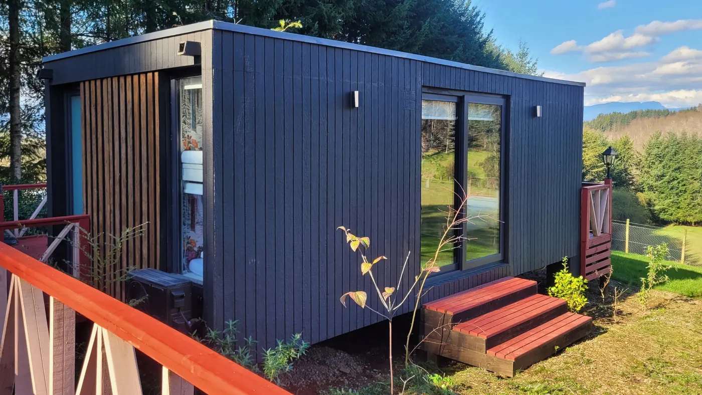 Tiny house con revestimiento negro, ventanales y escalera de acceso