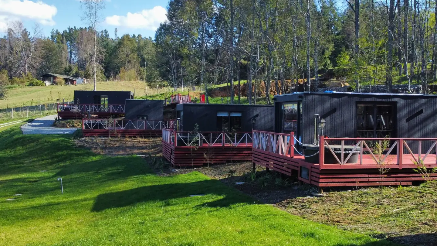 Tiny houses de Aslanhaus, Tinys Lefún, con decks de madera roja sobre la pradera junto al bosque