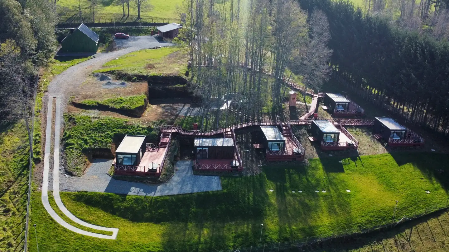 Vista aérea de las tiny houses de la etapa 1 de Aslanhaus unidas por una pasarela de madera junto al bosque