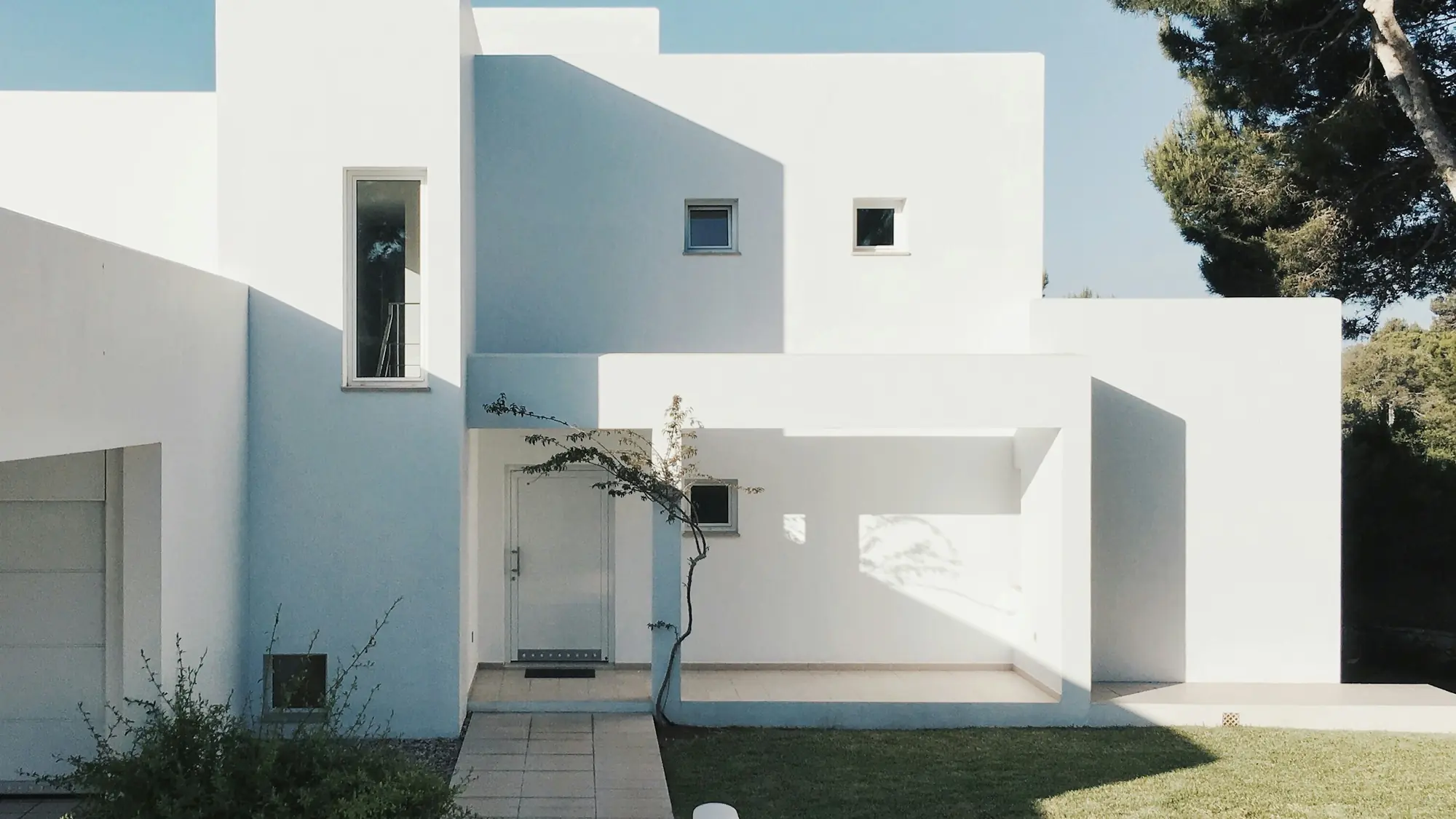 A low white stucco residence set behind a clean lawn and a mature pine.
