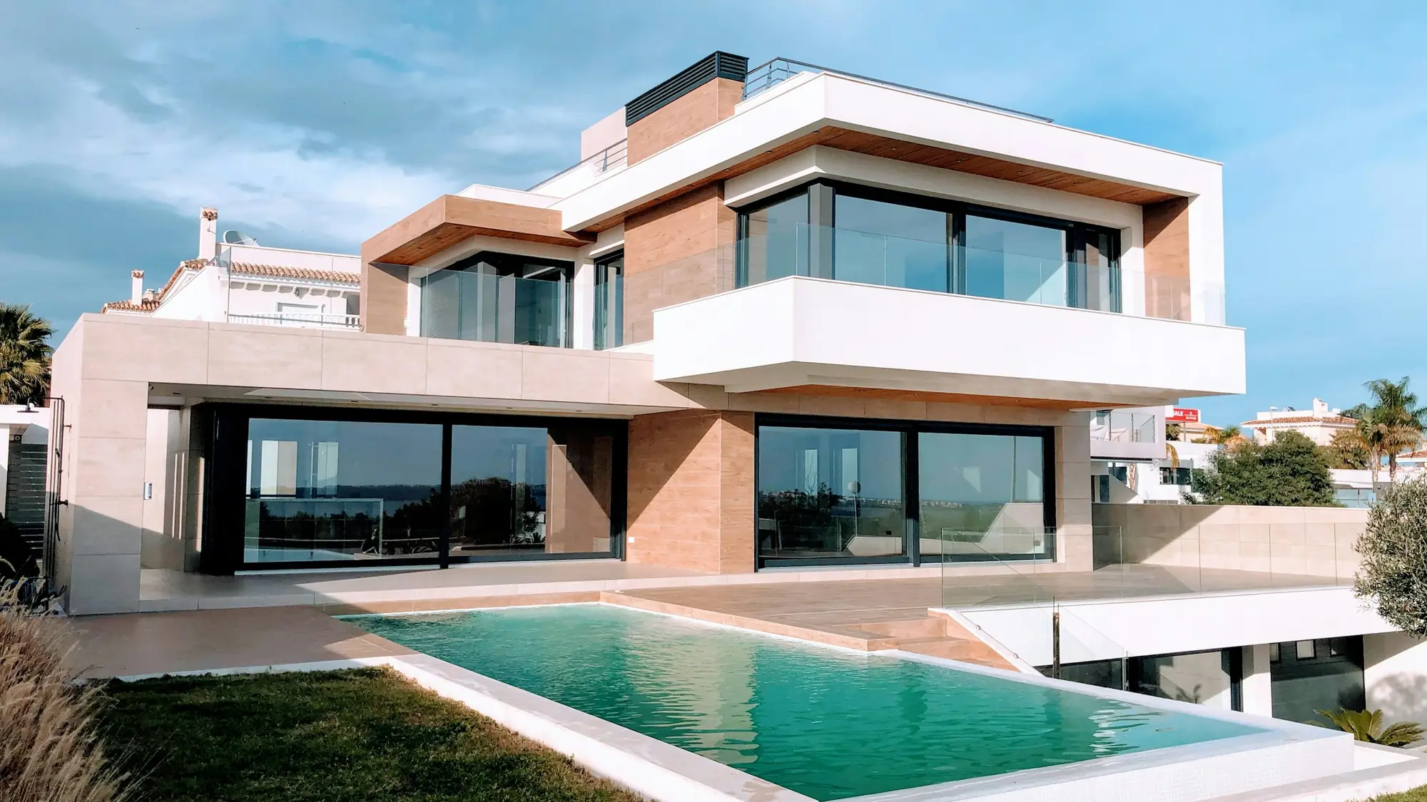 A contemporary residence in warm stone and white render, cantilevered over a lap pool.