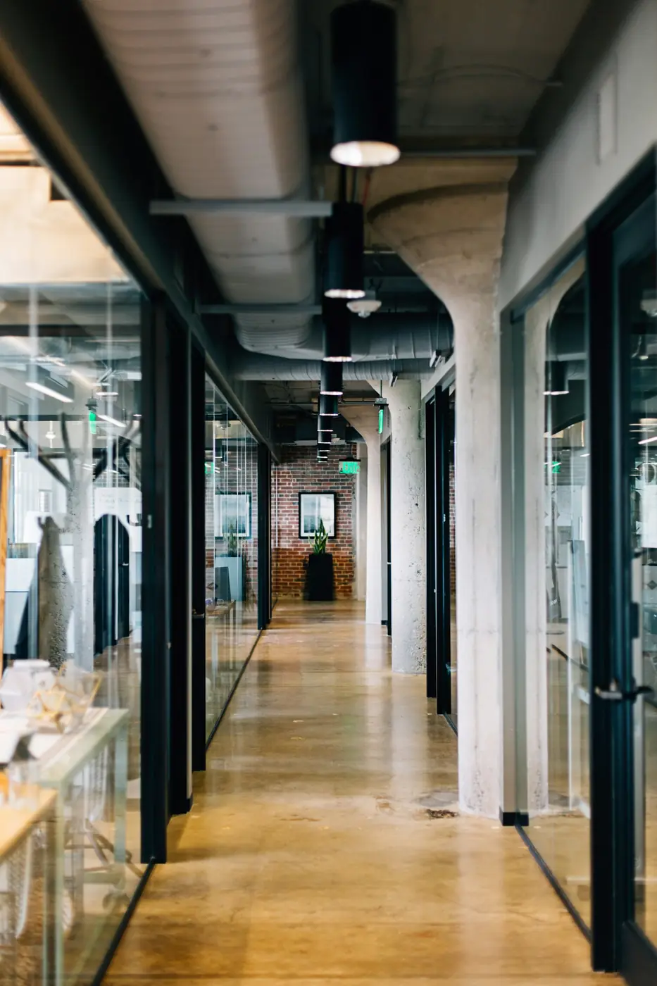 A long office corridor in glass and concrete with an exposed structural ceiling.
