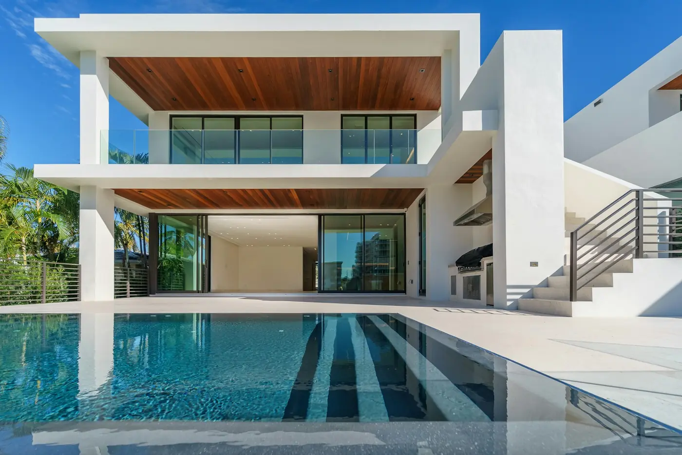A white and timber residence opening onto a lap pool framed by palms.