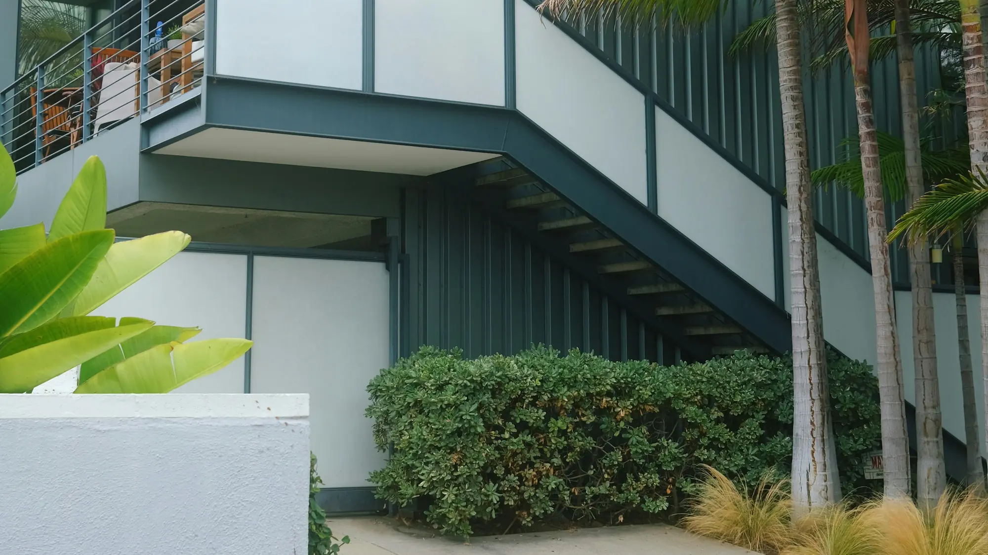 A modern California residence with a cantilevered balcony framed by palms.