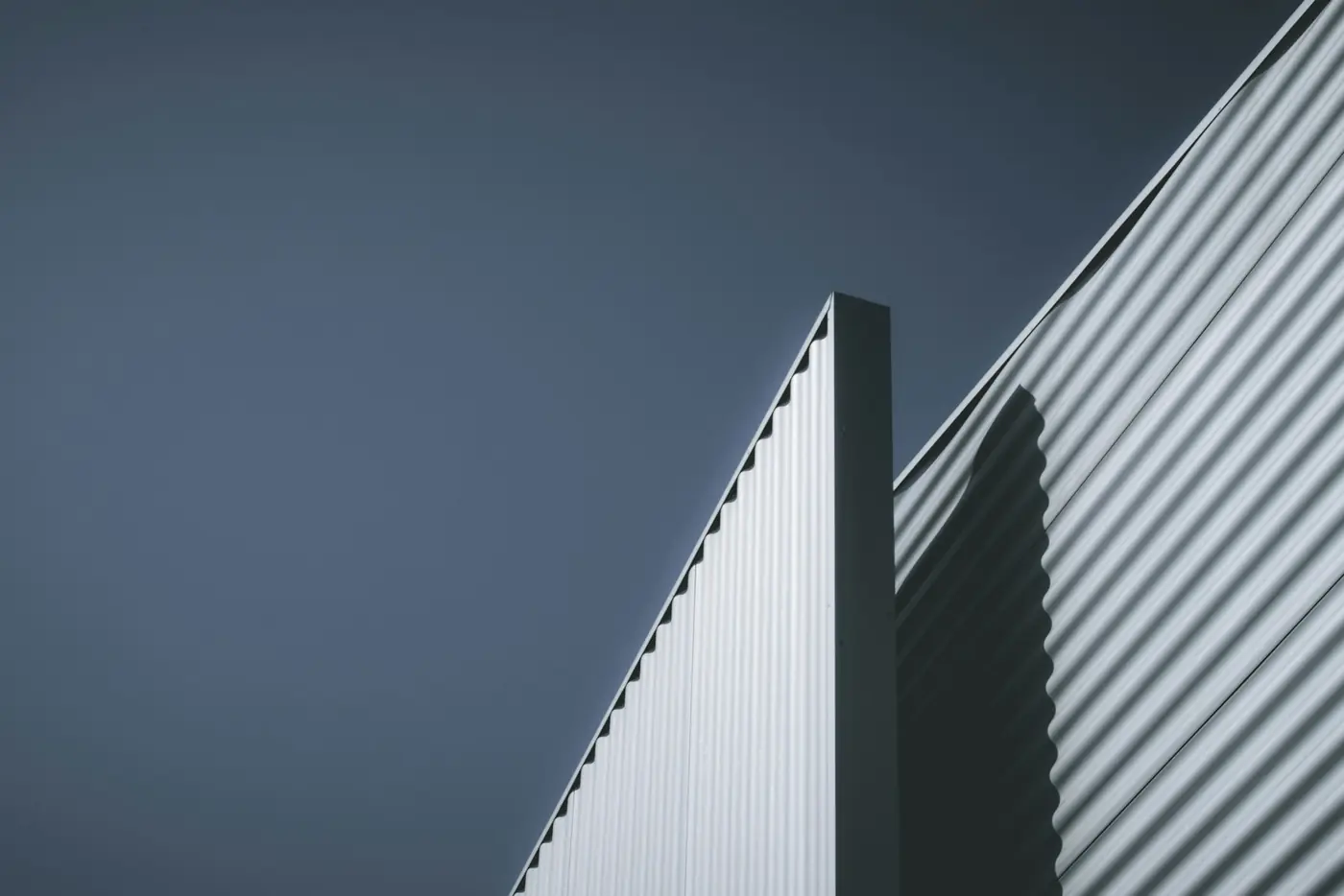 A ribbed metal facade cutting a hard diagonal against deep evening sky.