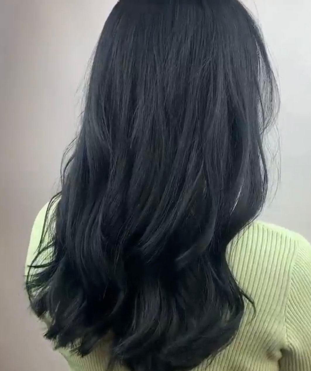 Dark layered hair against a neutral wall, back view.