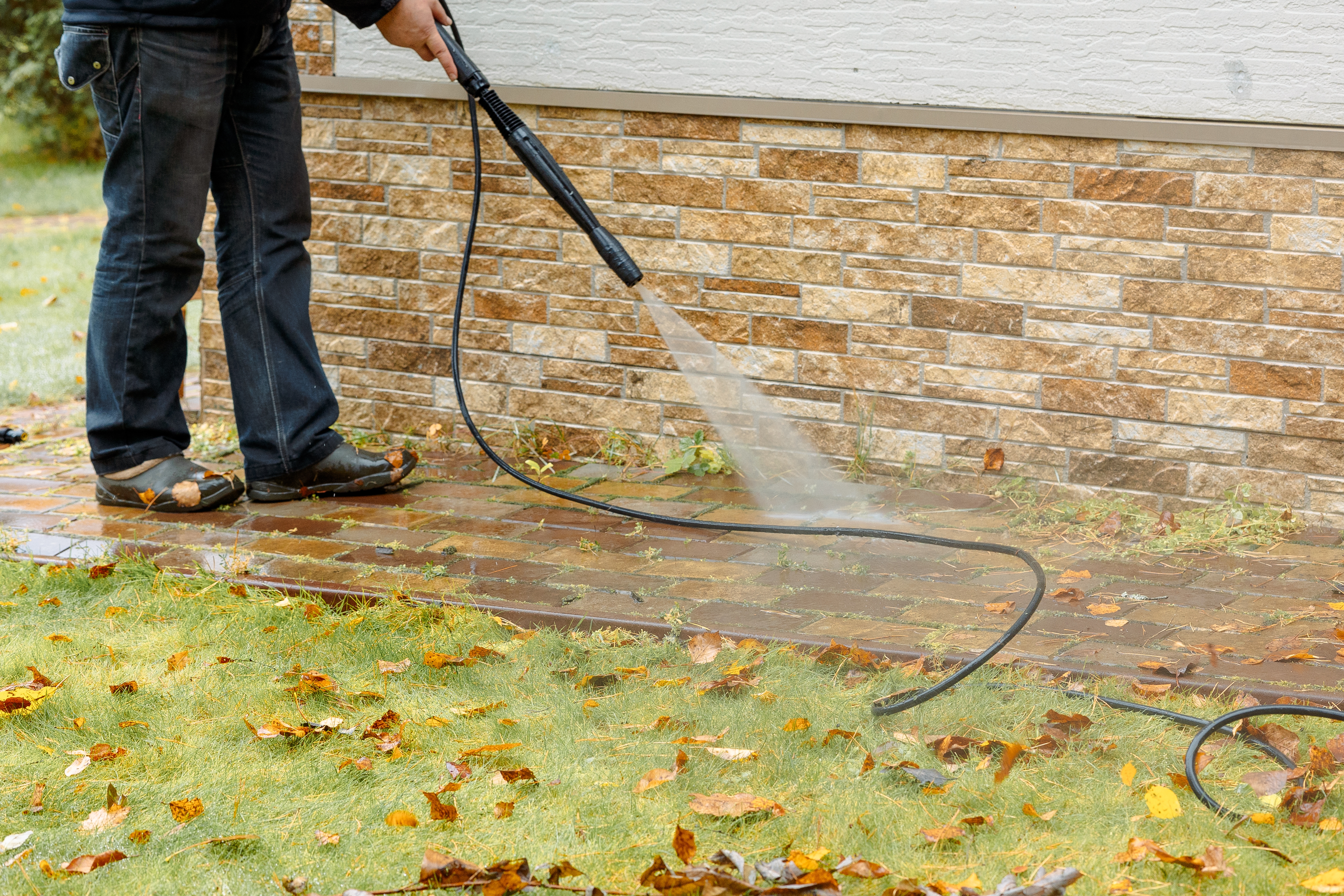 person power washing the brick foundation of a home