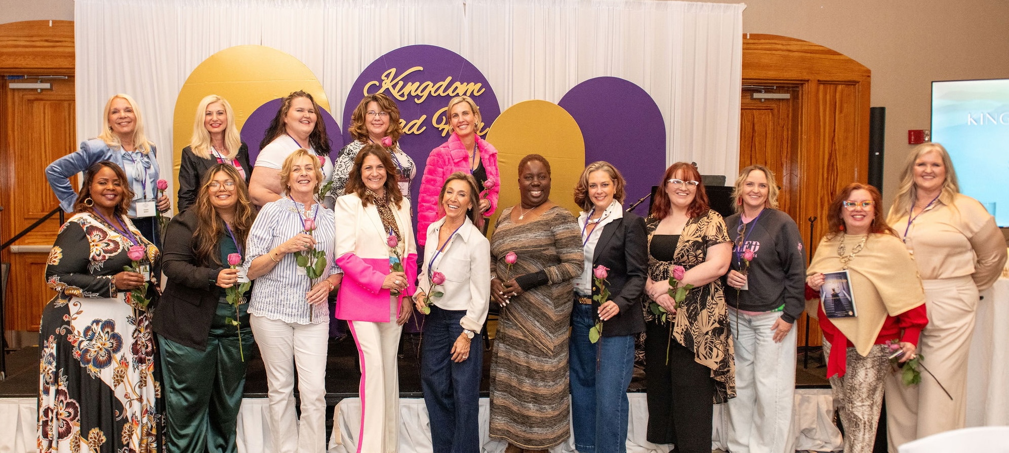 Kingdom LeadHERship Summit attendees gathered at the stage backdrop with roses