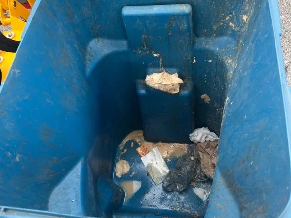 Inside view of a dirty blue plastic trash can with food scraps, wrappers, and general refuse accumulating at the bottom.