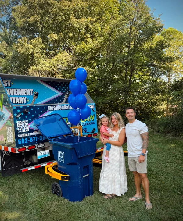 A family of three smiles in front of a blue trash can and a cleaning service truck with blue balloons.