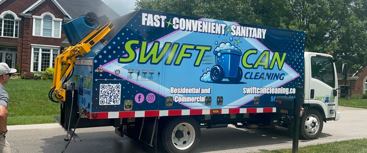 A Swift Can Cleaning truck with a blue and white wrap, actively cleaning a black trash can on a suburban street. A Swift Can Cleaning truck with a blue and white wrap, actively cleaning a black trash can on a suburban street.
