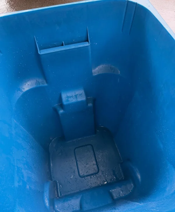 A close-up, high-angle view of the wet, empty interior of a bright blue plastic recycling bin.