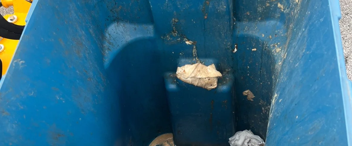 A top-down view inside a dirty, blue plastic waste bin containing food waste and trash.