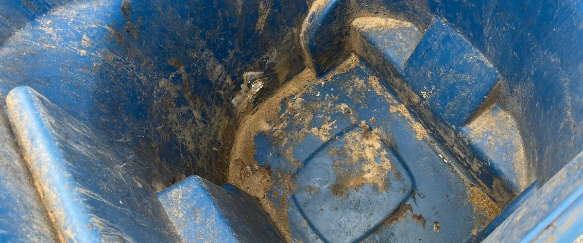 A close-up, high-angle view looking down into a dirty blue trash can with various garbage and liquid residue inside.