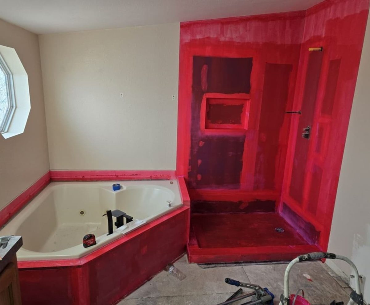 Red waterproofing membrane applied around a corner tub and shower.