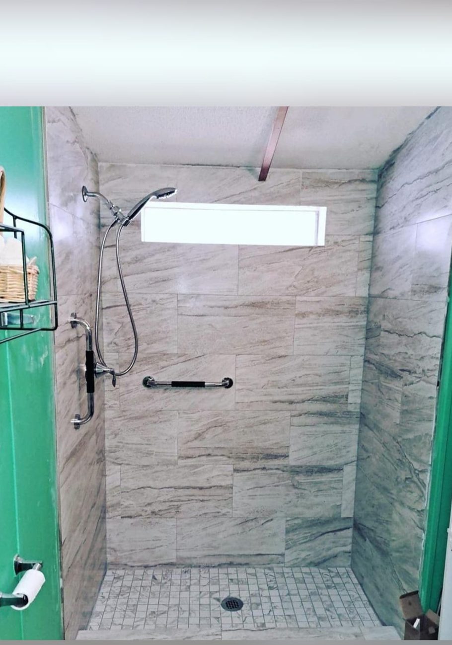 Walk-in shower with stone-look tile, grab bars, and a handheld showerhead.