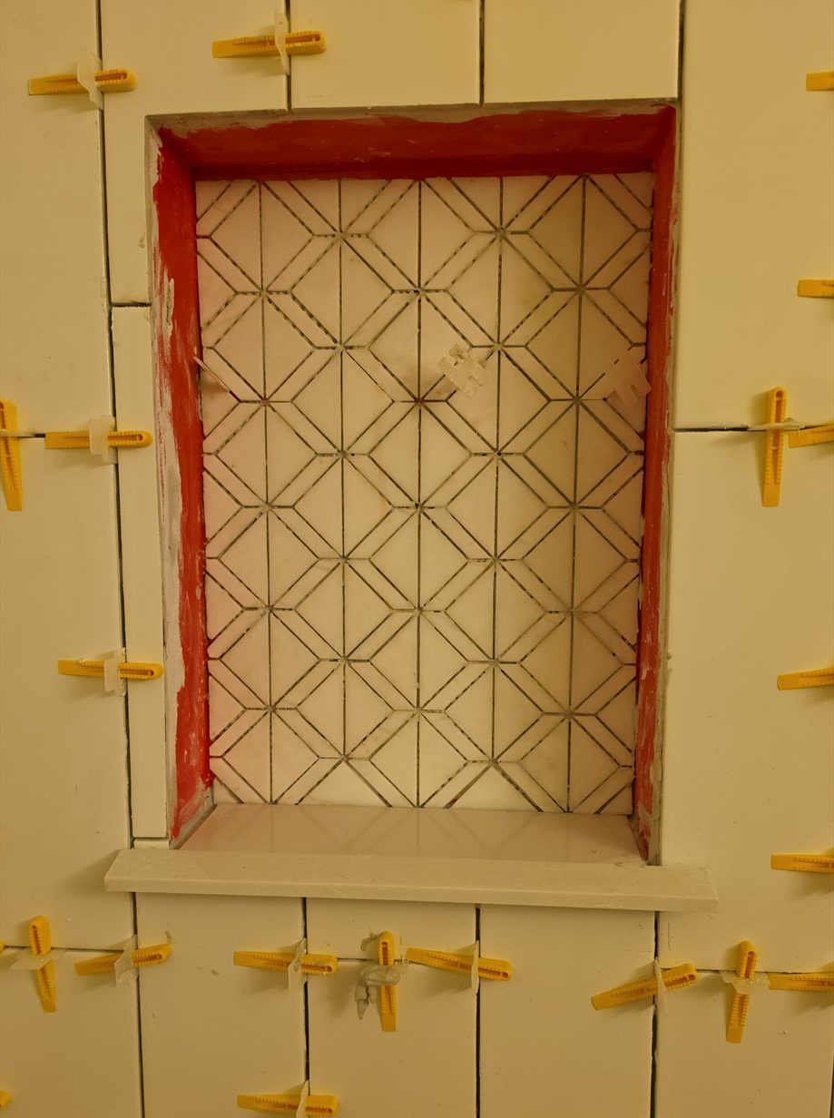 Patterned shower niche surrounded by white vertical tile during installation.