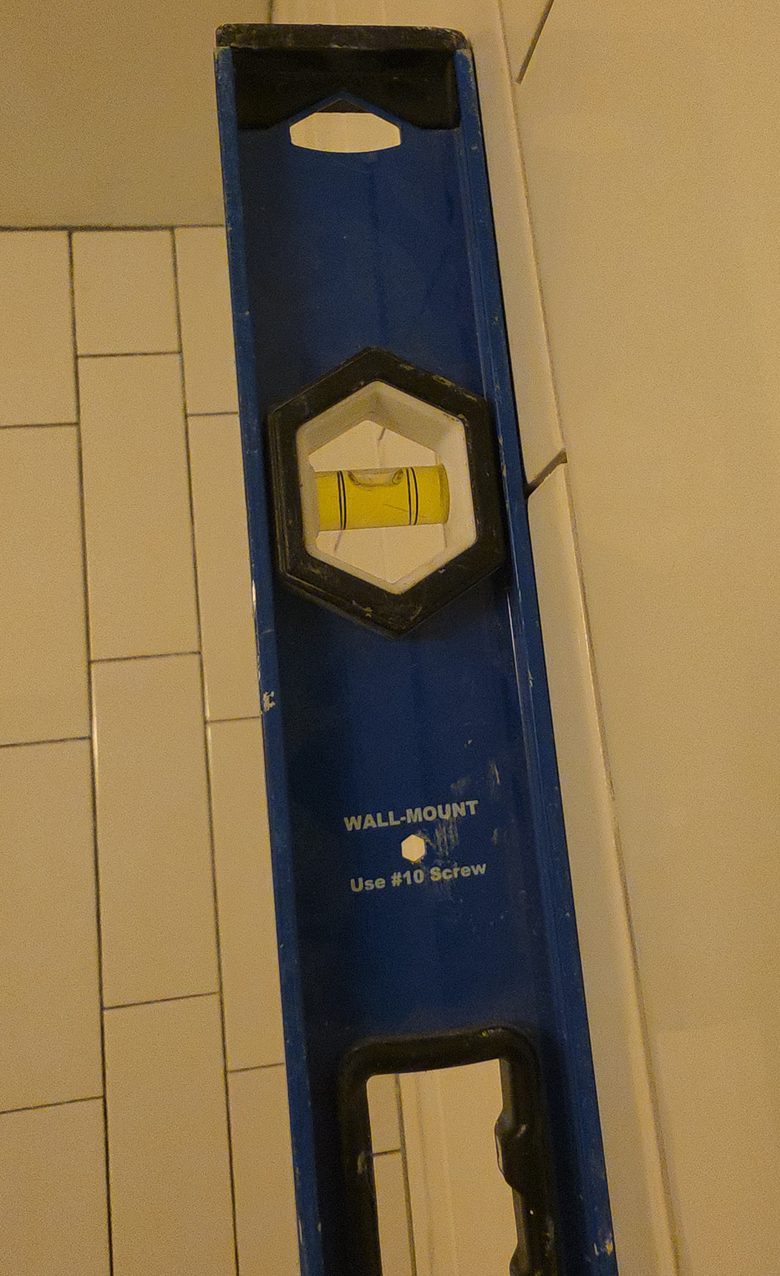 Level held against a tiled shower wall to check alignment.