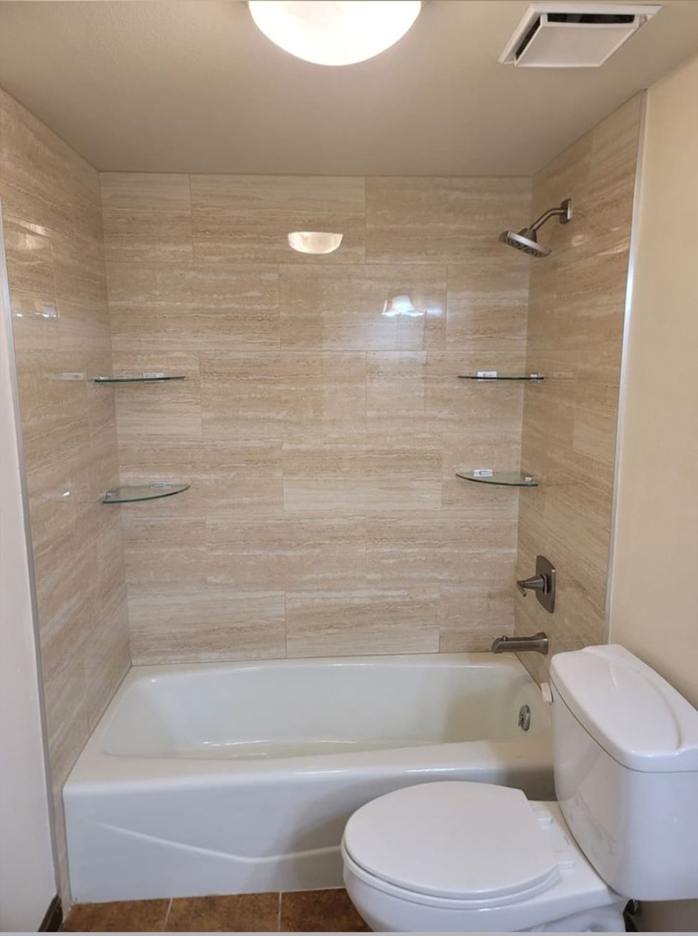 Tiled bathtub surround with stone-look wall tile and corner glass shelves.