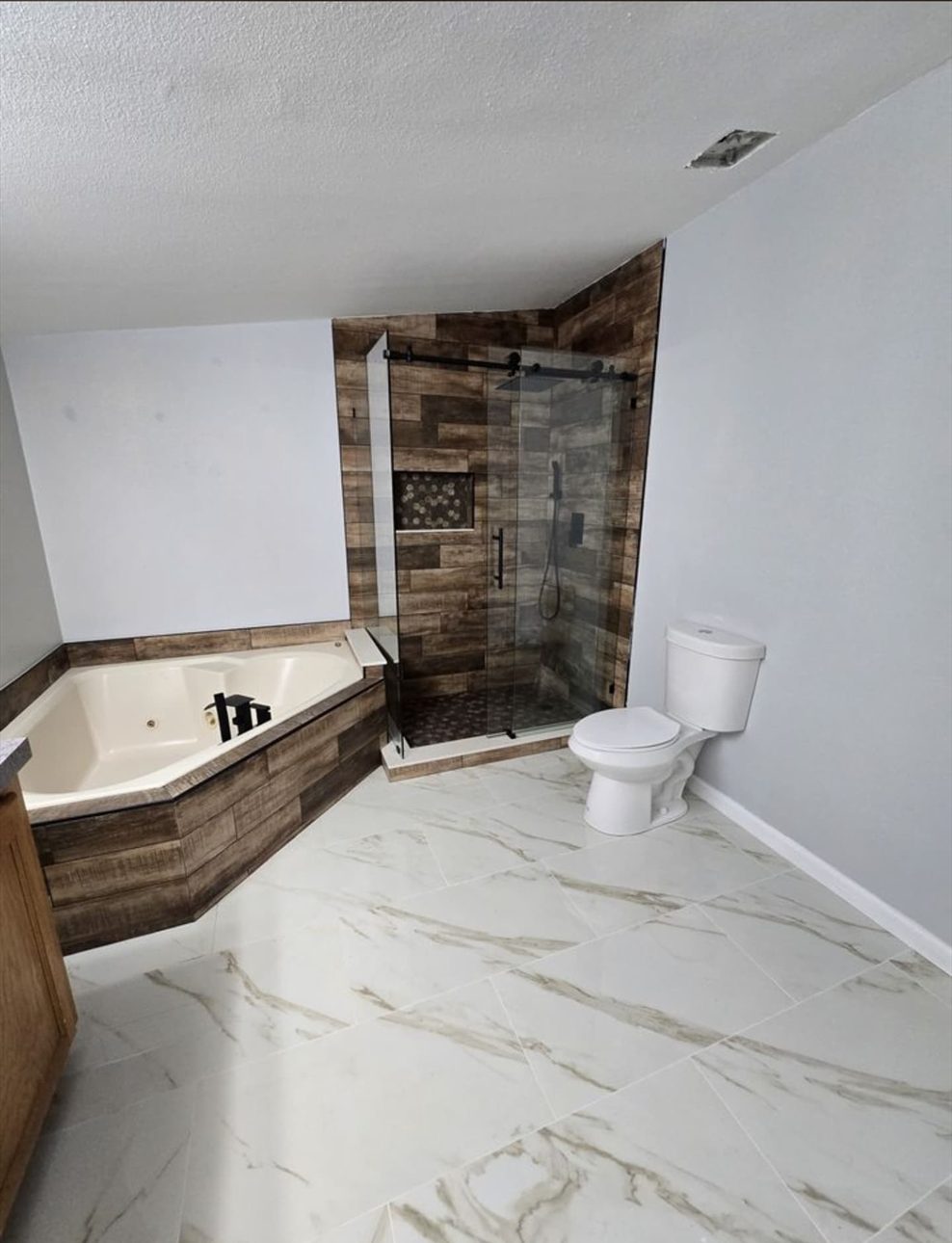 Bathroom with a corner tub, glass-enclosed shower, wood-look tile, and large-format floor tile.