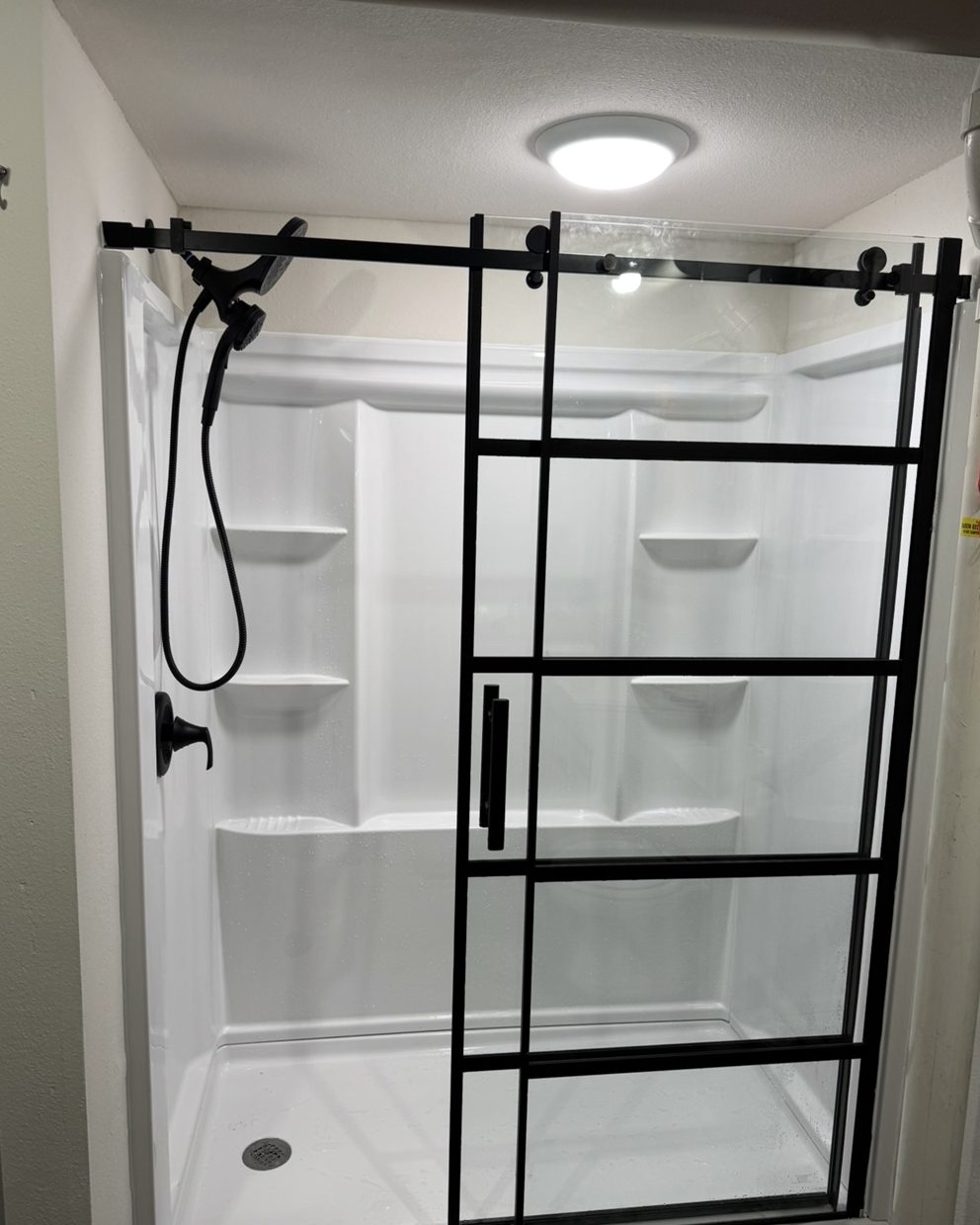 White shower with a black framed sliding glass door and matte black fixtures.