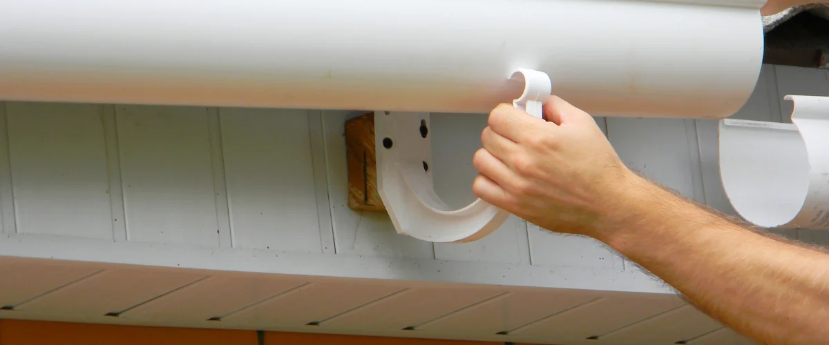 Installing PVC rain gutter bracket on residential home exterior. Installing PVC rain gutter bracket on residential home exterior.