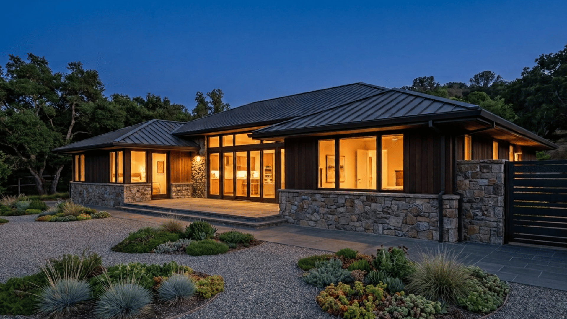 Alamo home at blue hour with warm interior light, stone base, paver walkway, and fire-wise garden groupings