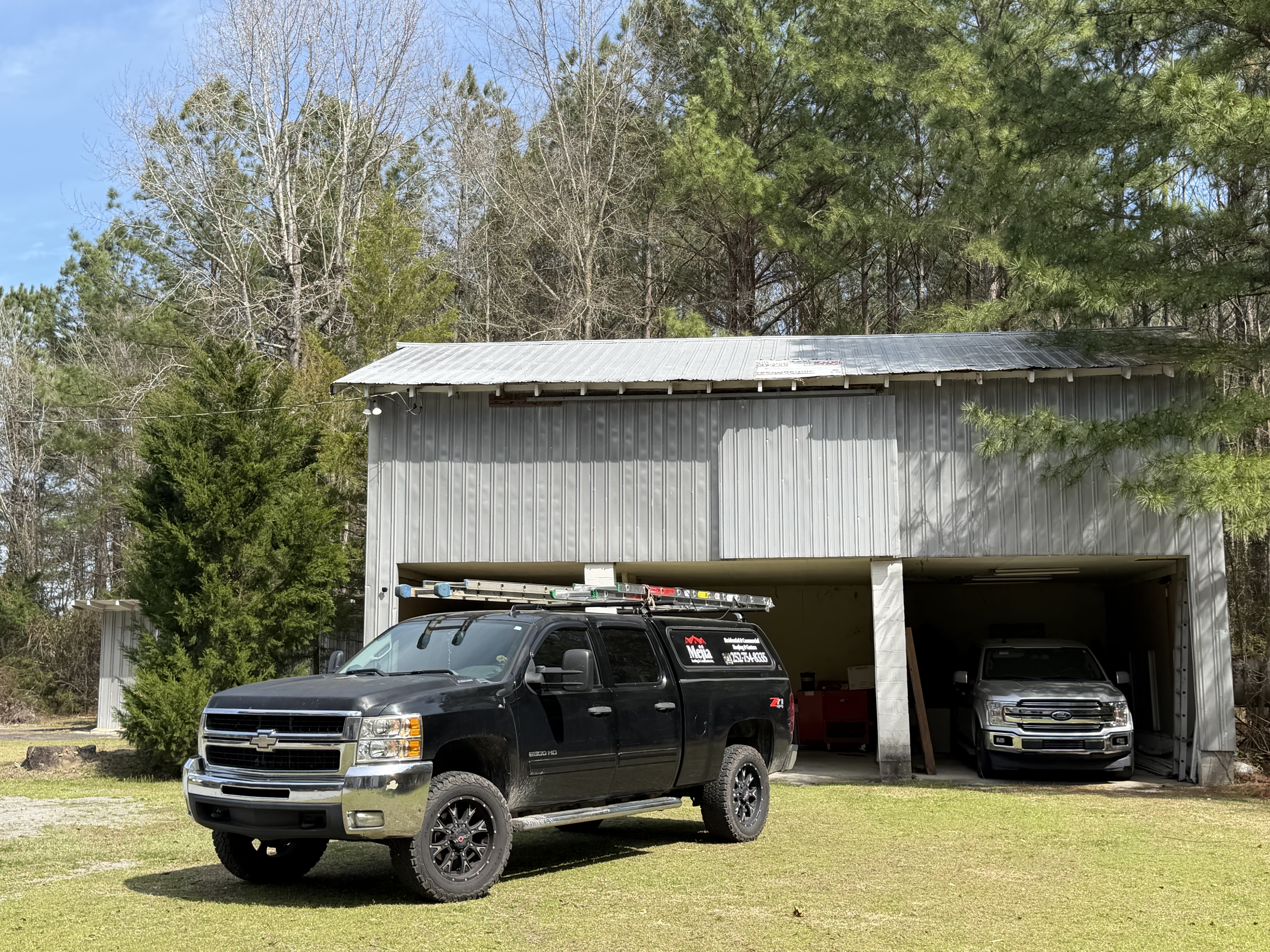Detached garage with a metal roof and a work truck with a ladder rack