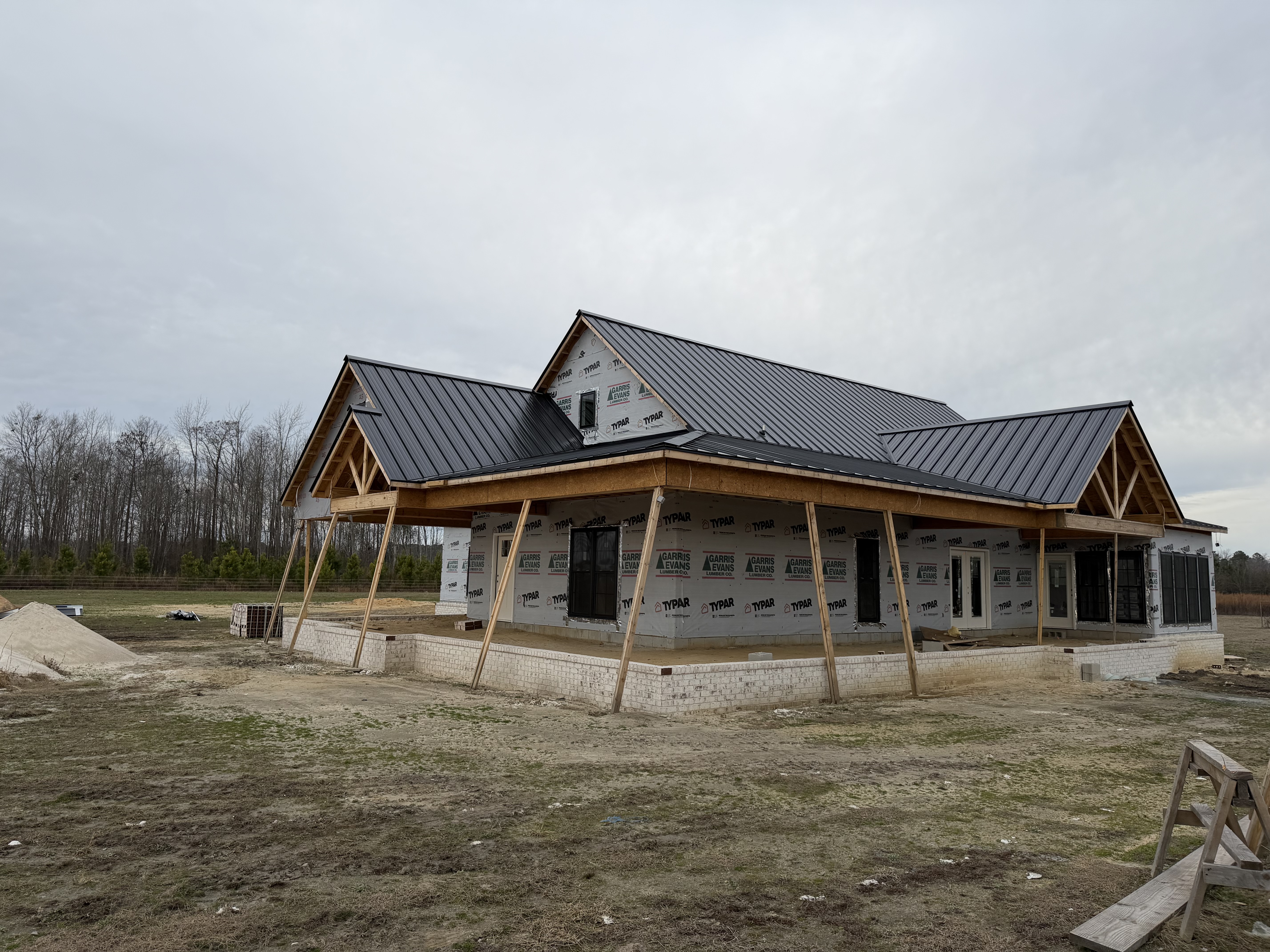 New construction farmhouse with a metal roof installed over the wrapped frame and front porch