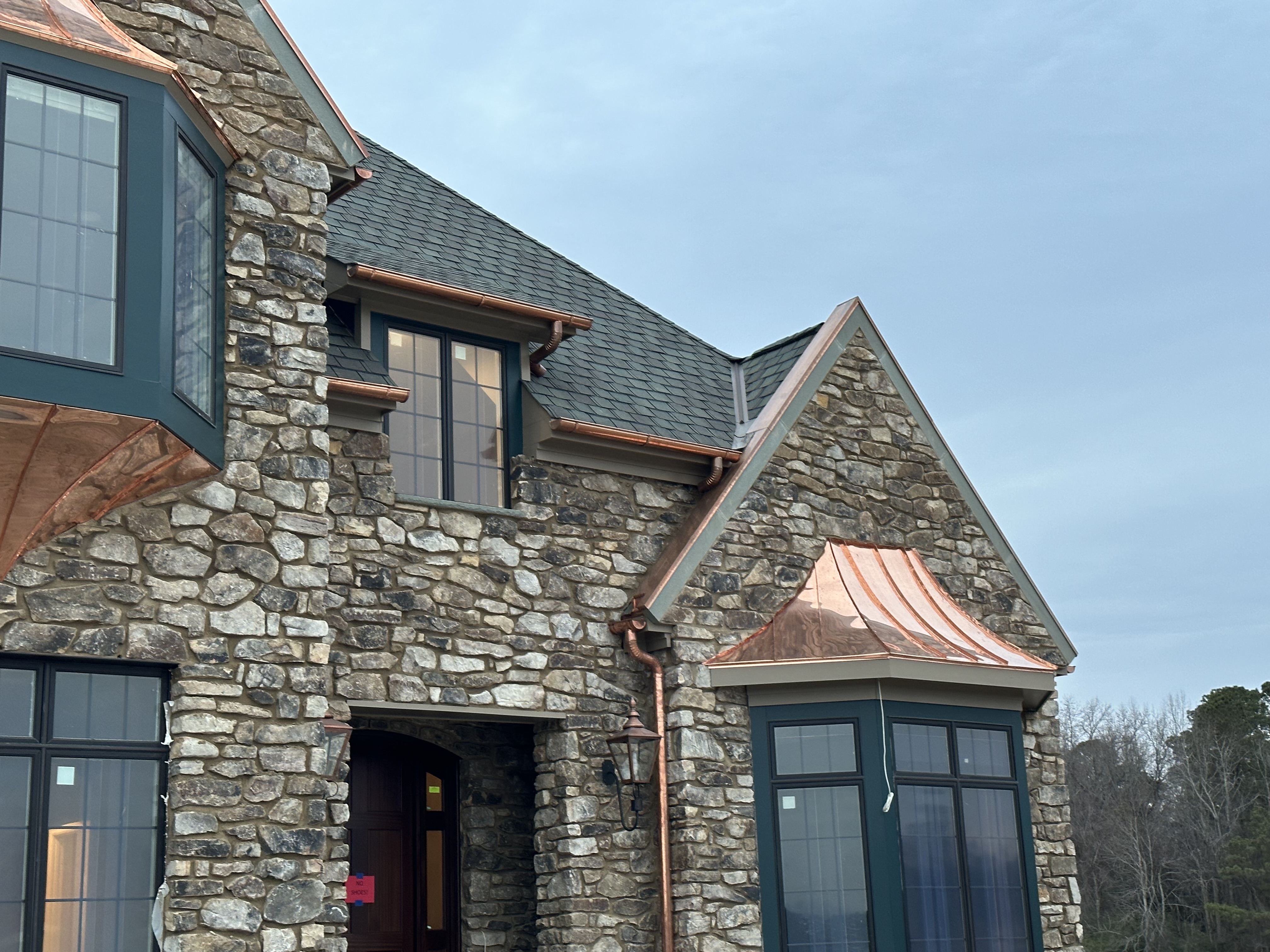 Stone house with a gray shingle roof and a copper-roofed bay window