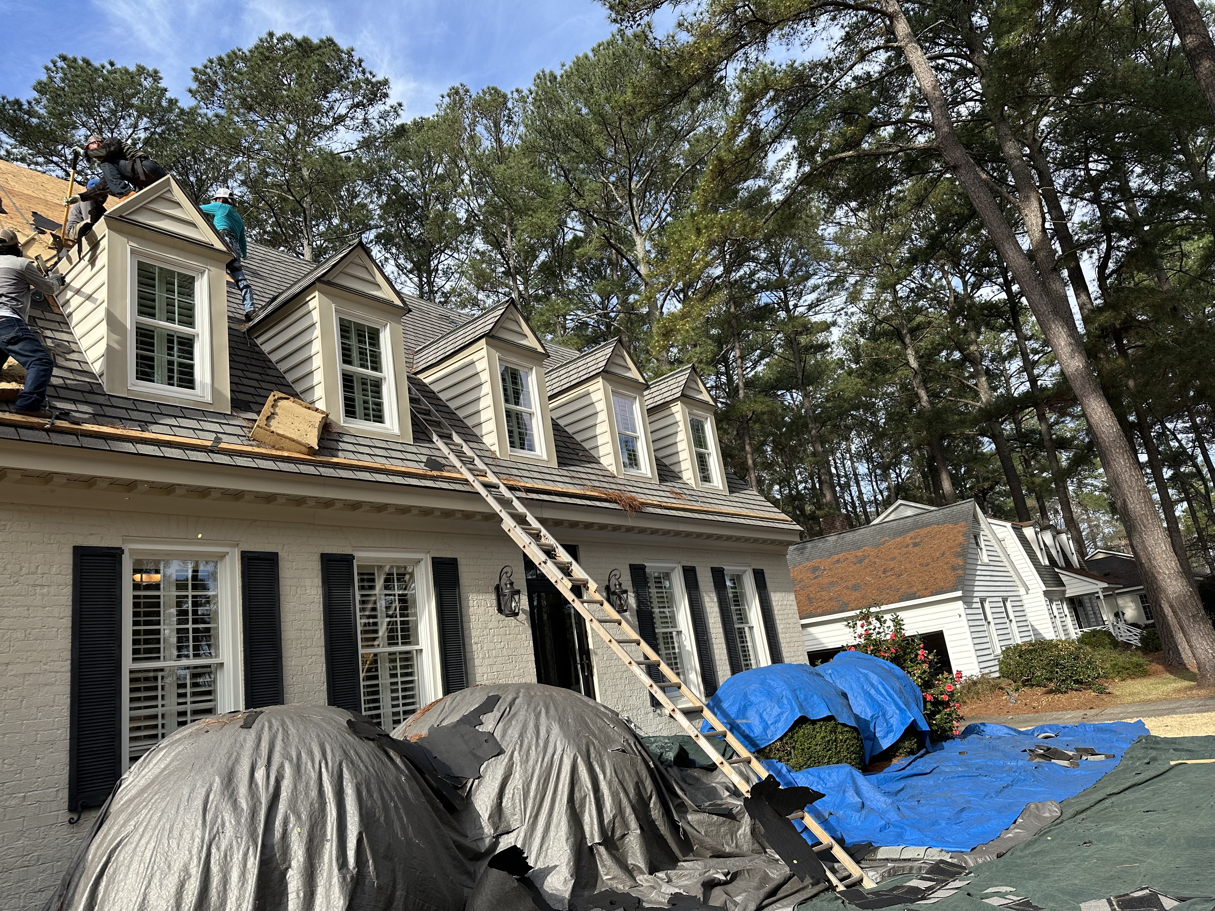 Roof tear-off underway on a two-story home, with tarps protecting the landscaping