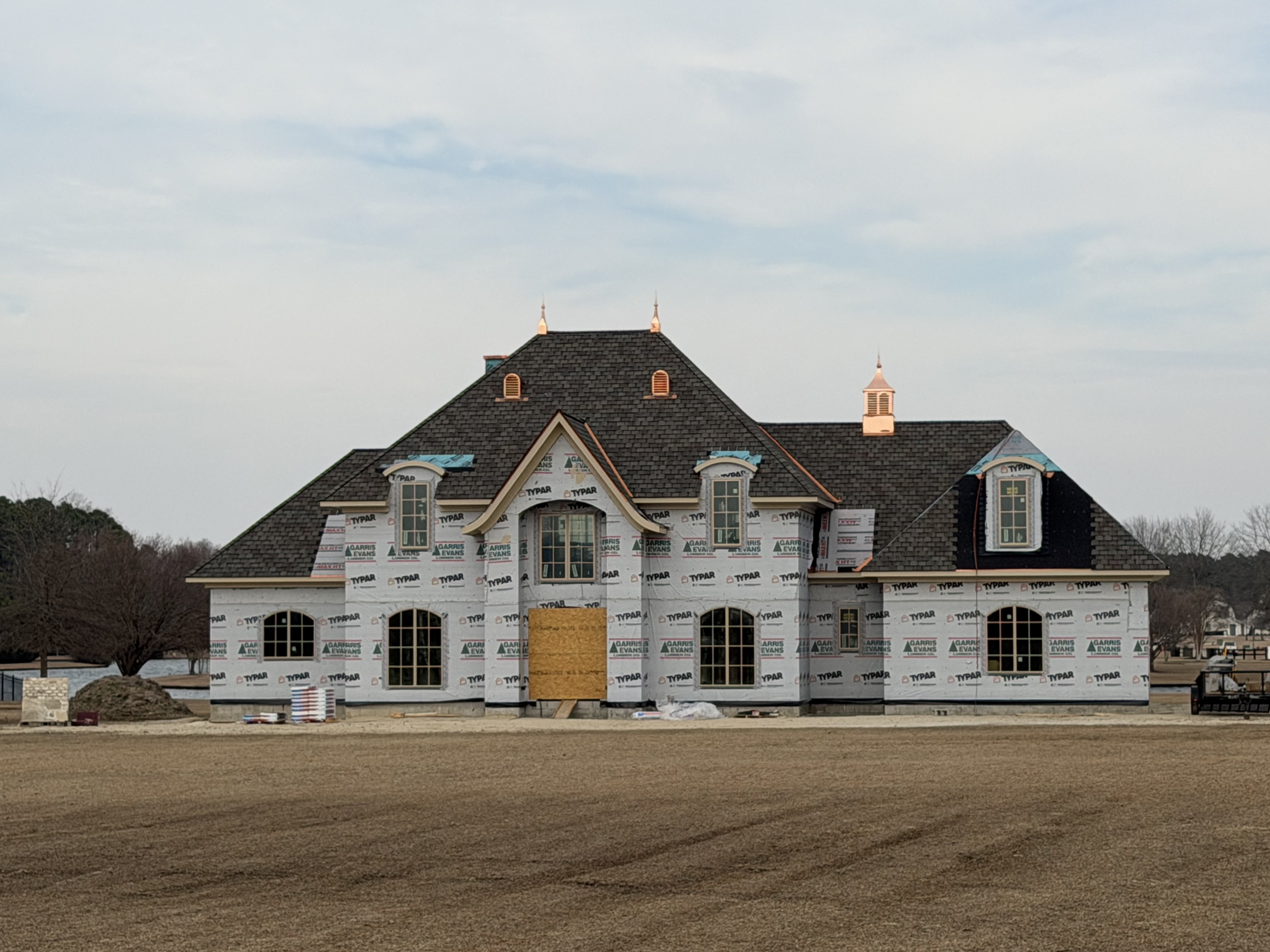 Large new-construction home with a dark shingle roof and copper cupola