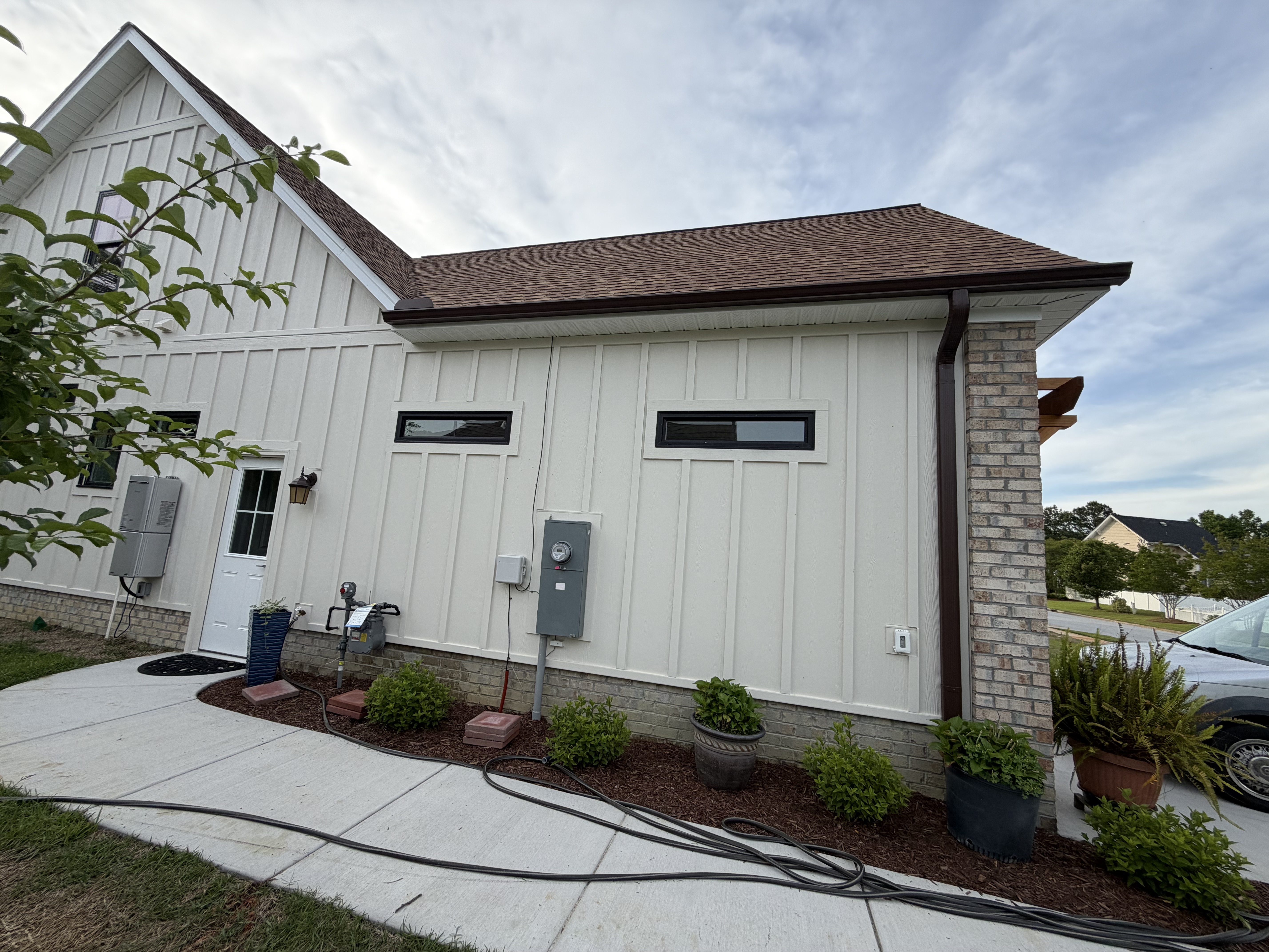 Side of a board-and-batten home with a brown shingle roof and gutters