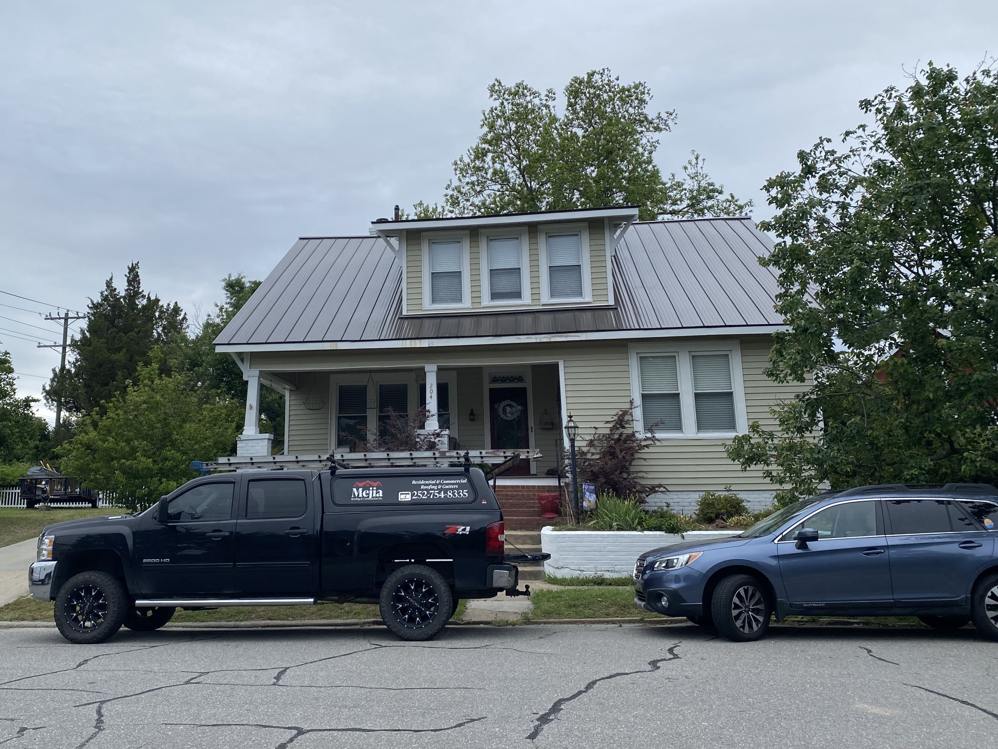 Home with a metal roof and front porch, with trucks in the driveway