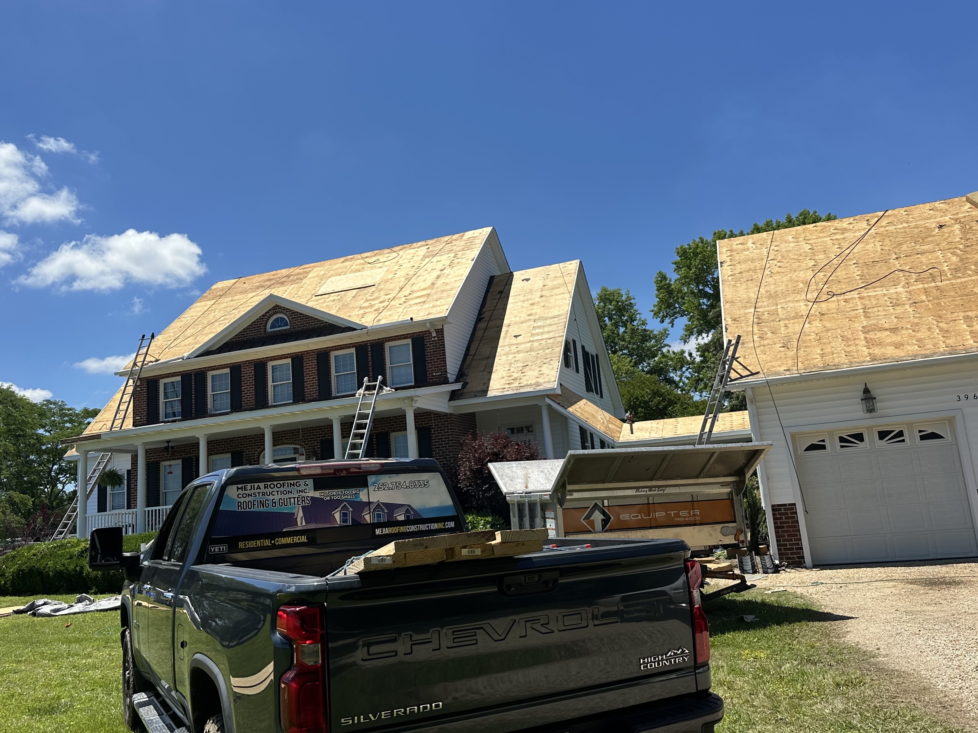 New roof decking going onto a two-story home, with work trucks parked out front