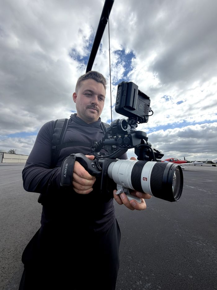 Drew Vernon holding a cinema camera on an airfield