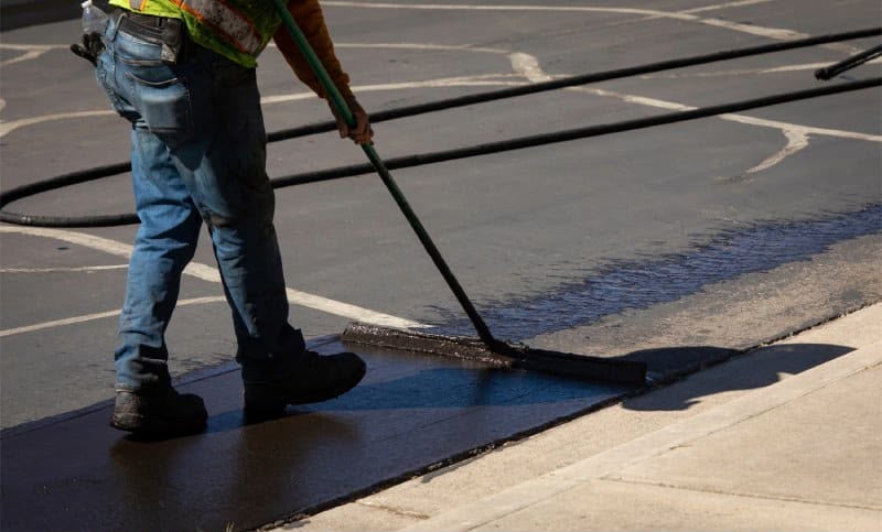 Elite crew member working sealer into the asphalt pores with a broom
