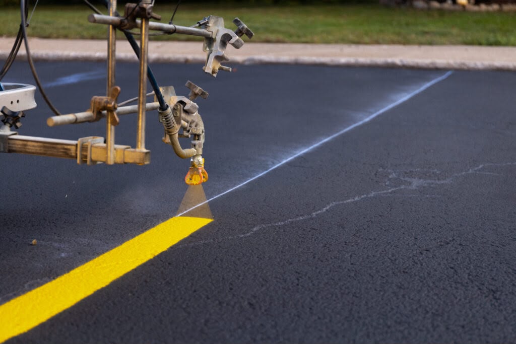 Elite striping machine spraying a fresh yellow line along a chalk line