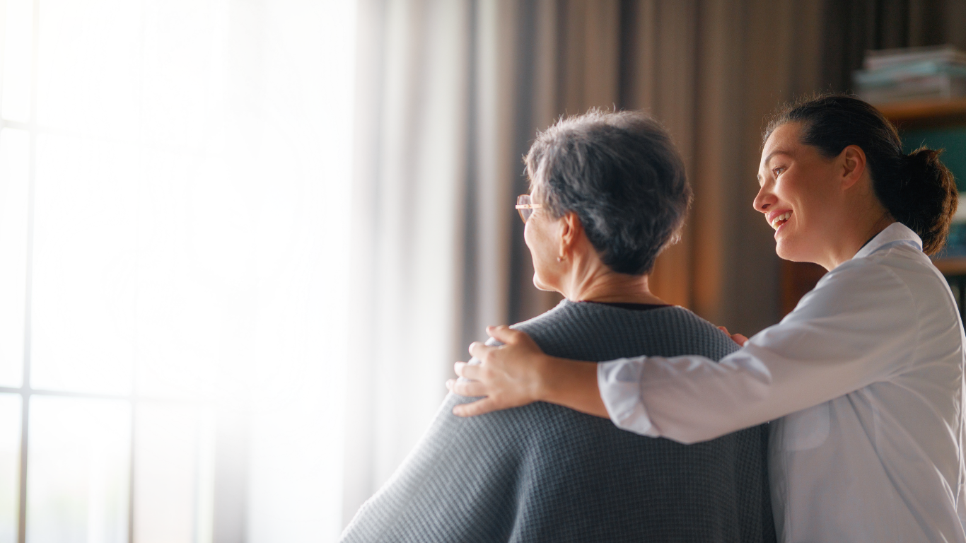 A clinician smiling with her arm around an older woman at home
