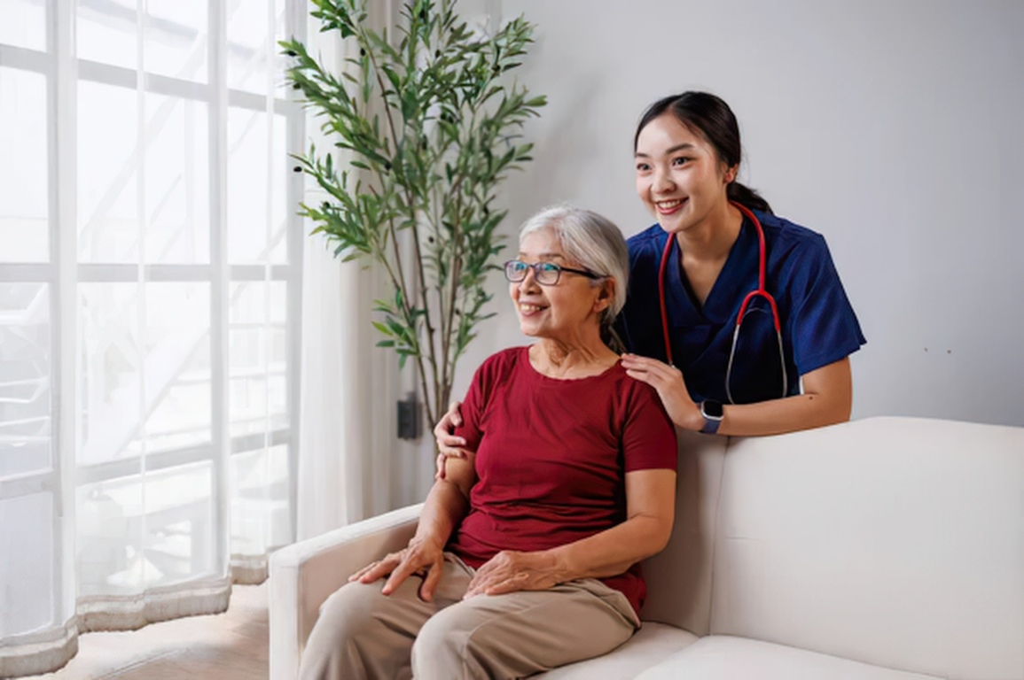 A smiling nurse with her hands on an older woman's shoulders at home