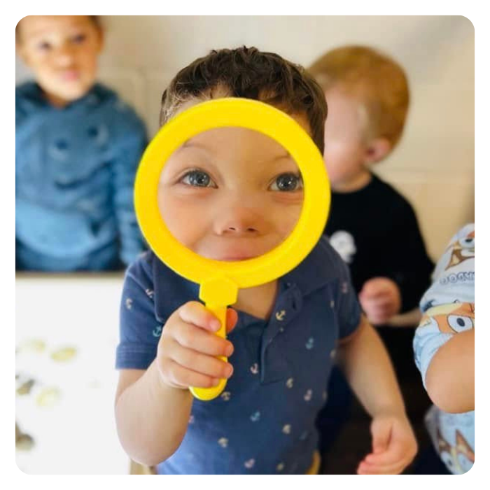 child looking into yellow magnifying glass 