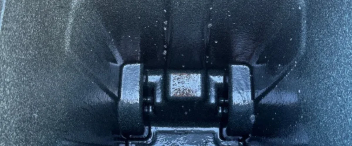 Close-up of a dark metal hinge with water droplets, showing texture and light reflections.